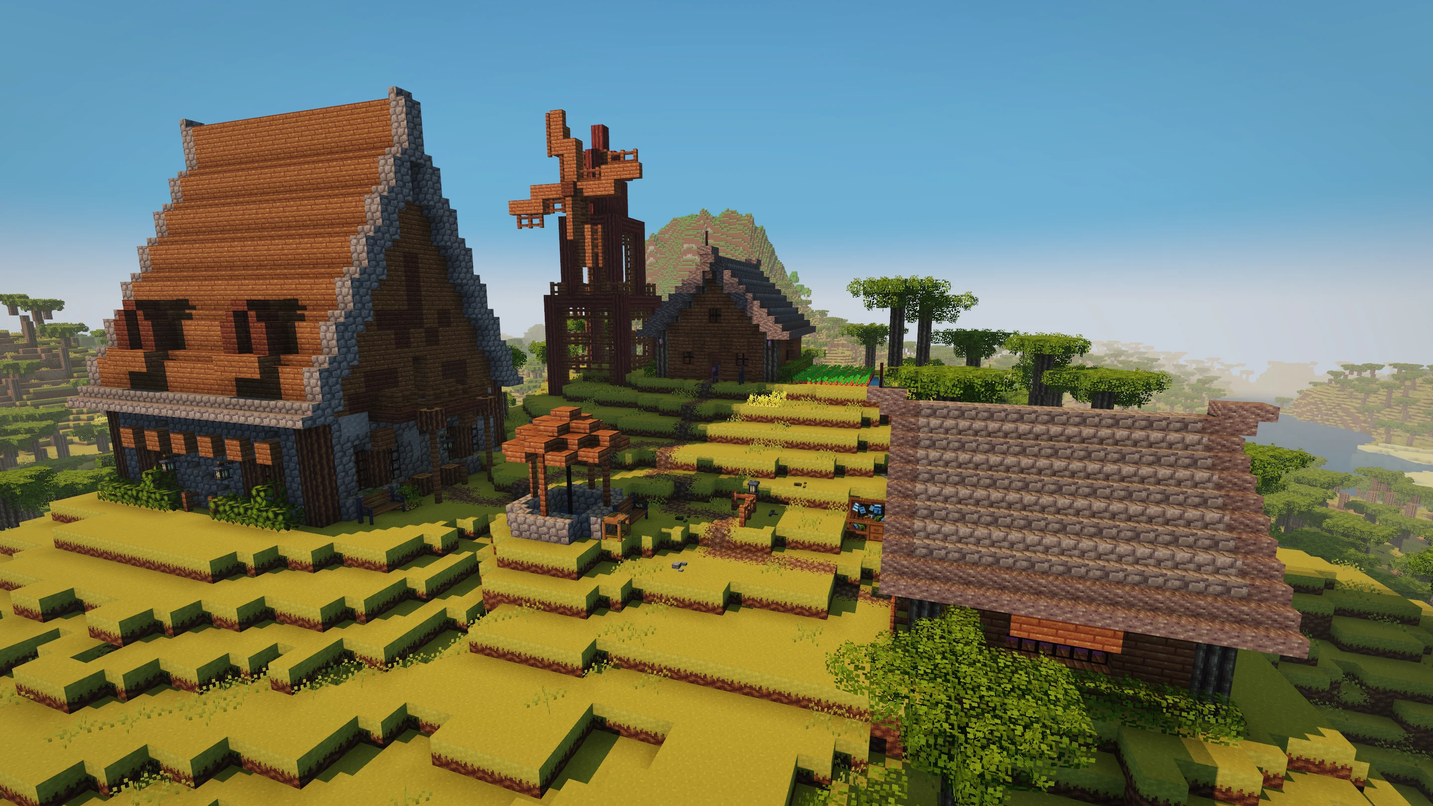 A player-built village spread across a hillside, with timber houses, gardens, a windmill, and a well
